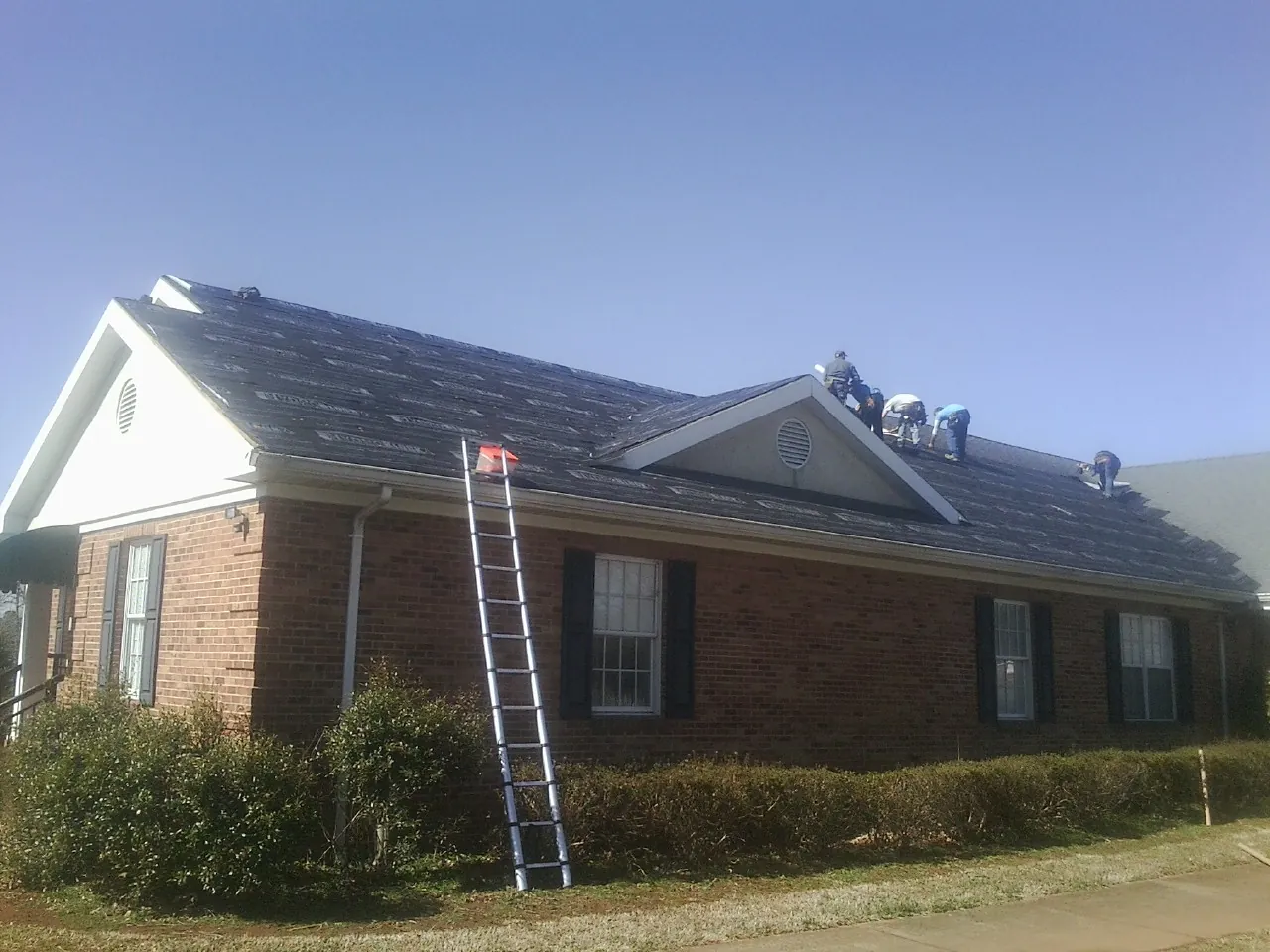 Crew tearing shingles off a brick ranch roof with a ladder set — Metal Roof Repair work by our crew in Wappingers Falls