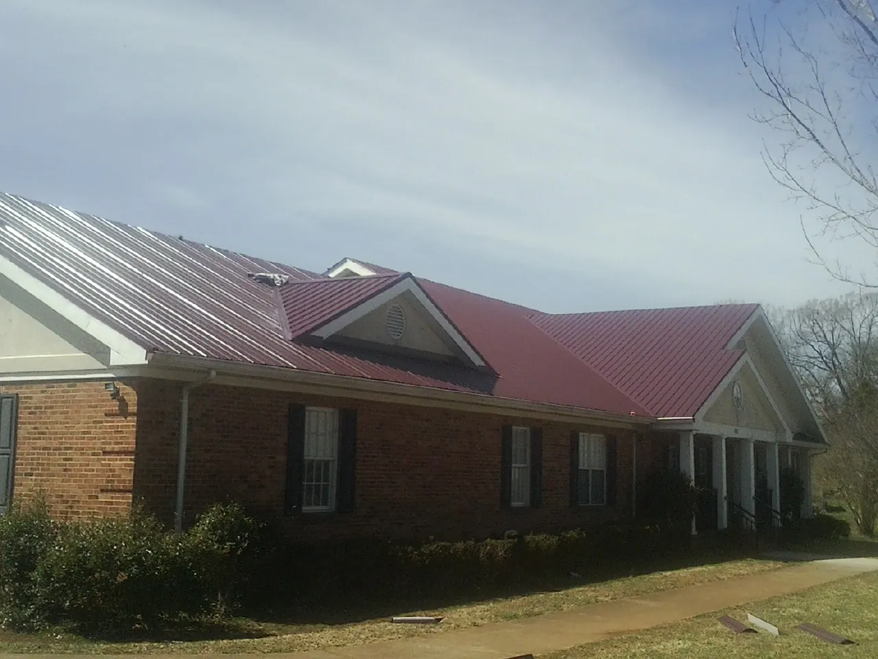 Red metal roof with gabled entries on a long brick building, from a Hail Damage Roof Repair job in Wappingers Falls