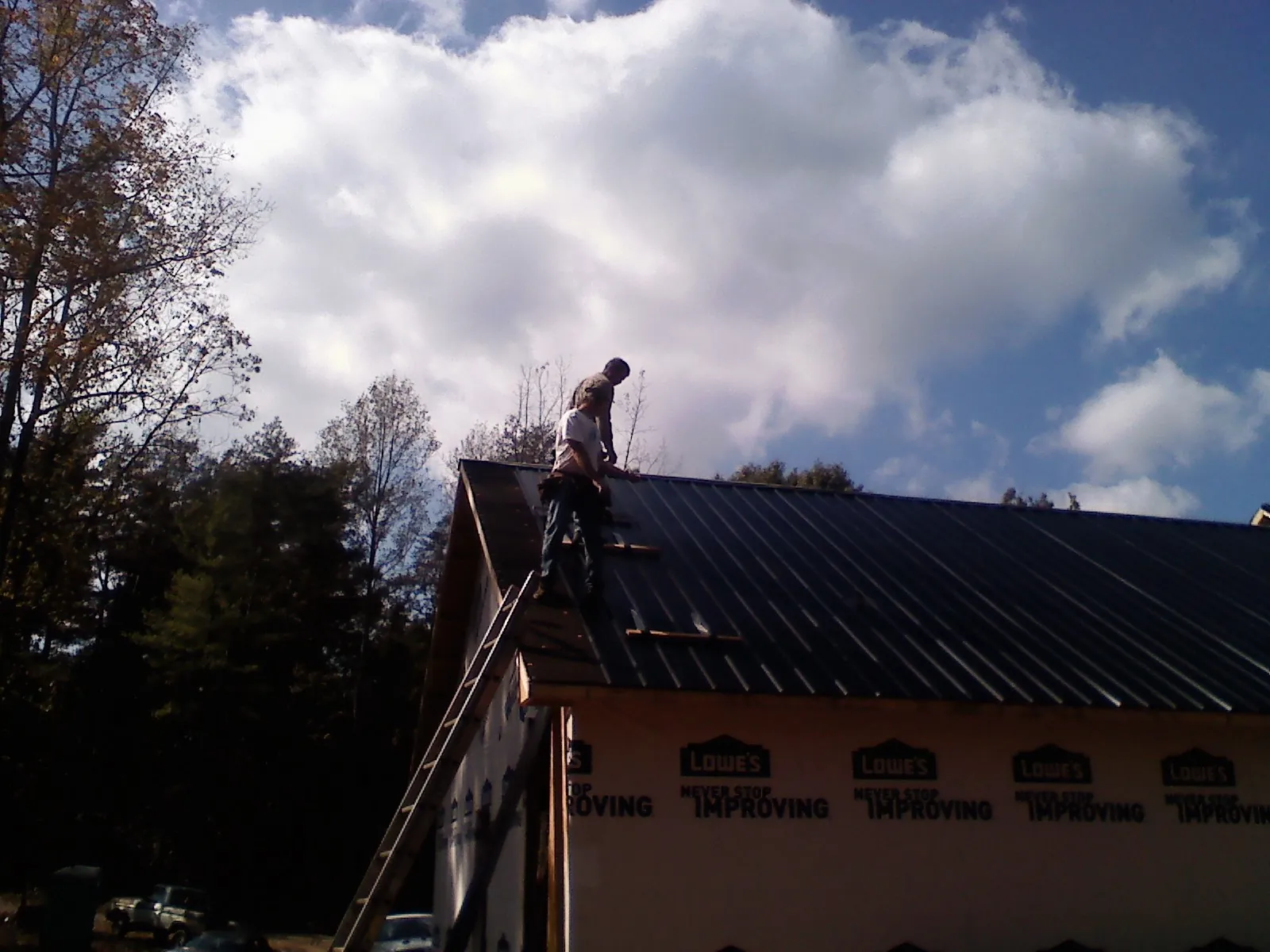 Roofer fastening dark metal panels high against a cloudy sky, from a Roof Inspection job in Wappingers Falls
