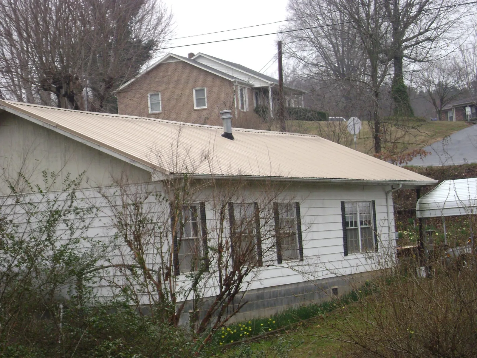 Tan metal roof on a white sided house set into a hillside — Commercial Roofing by Roofing Brothers in Wappingers Falls